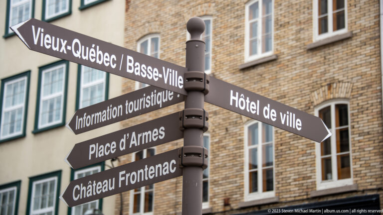 Brown directional signpost pointing to Vieux-Québec, Basse-Ville, Hôtel de ville, tourist information, Place d’Armes, and Château Frontenac.