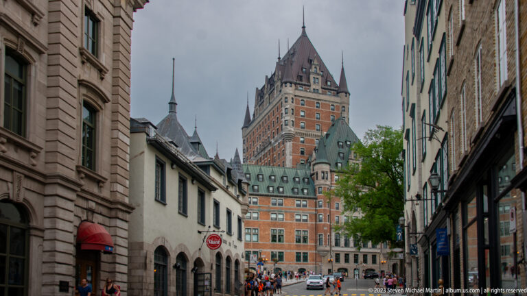 Fairmont Le Château Frontenac rises above a narrow Old Quebec street lined with lower historic buildings and pedestrians.