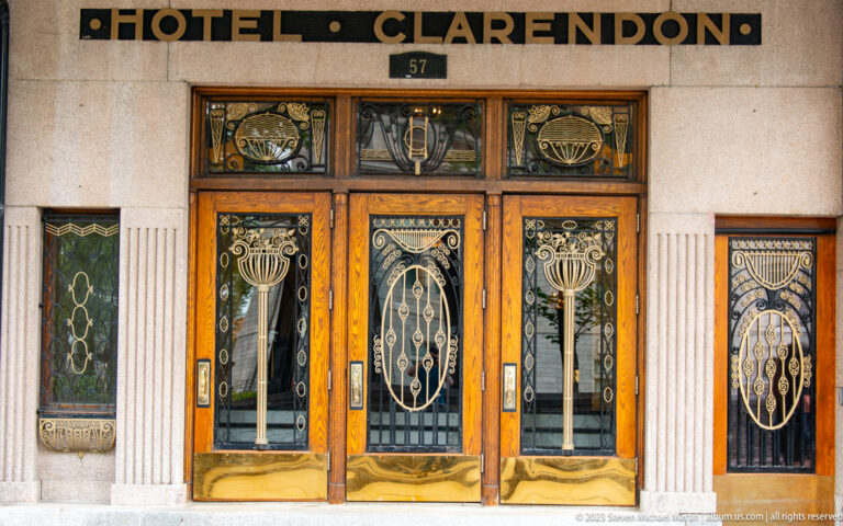 Ornate wooden and glass entrance doors beneath the word CLARENDON and street number 57, with decorative metalwork in each panel.