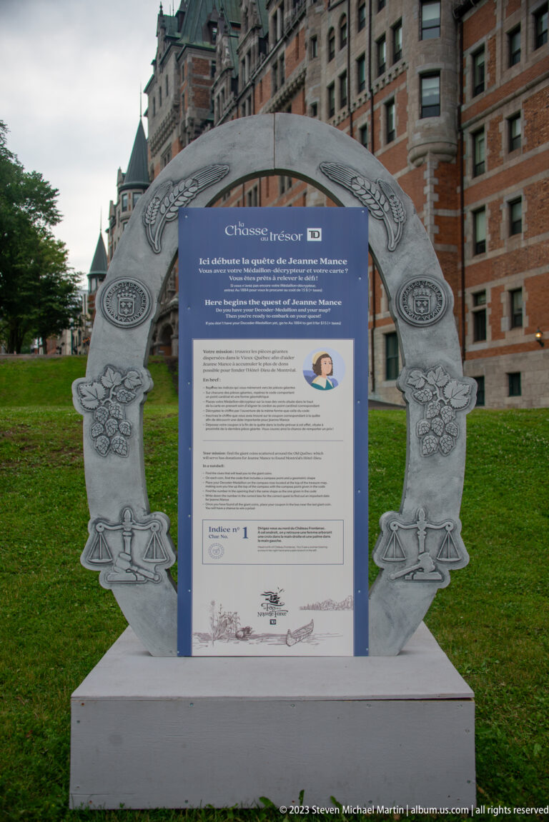 Blue historical interpretive panel set inside a large decorative gray frame on lawn, with Château Frontenac behind.