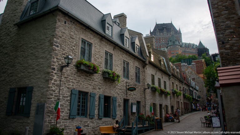 Stone Lower Town buildings with shutters and flower boxes line a narrow street, with Château Frontenac rising high on the bluff.