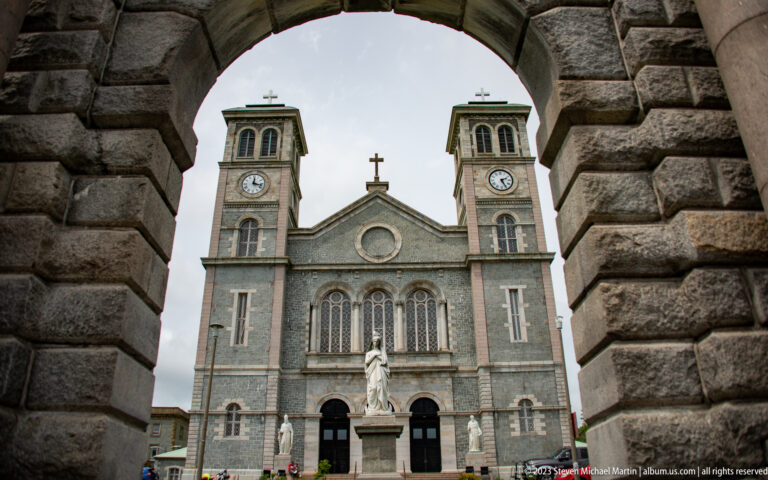 Basilica-Cathedral façade and central statue framed through a massive stone arch in the forecourt gateway.