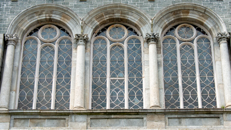 Three tall arched cathedral windows divided by stone columns and filled with looping geometric tracery.