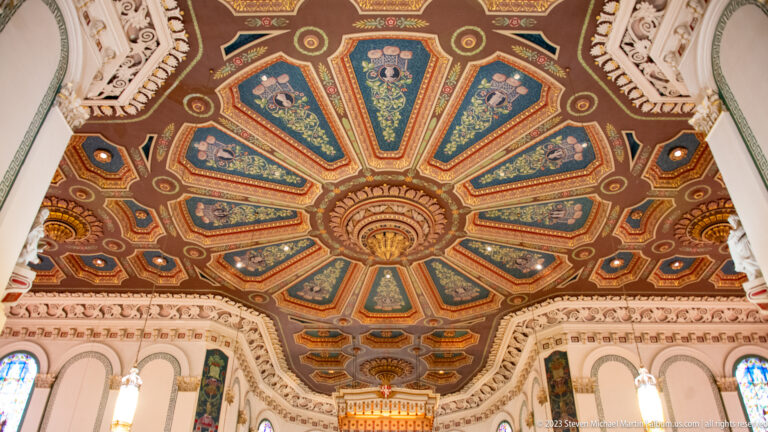 Ornate cathedral ceiling with radial green, blue, red, and gold painted panels surrounding a central rosette.