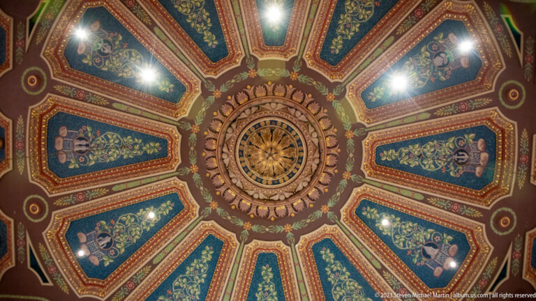 Ornate circular ceiling medallion surrounded by radiating blue-green, red, cream, and gold painted decorative panels.