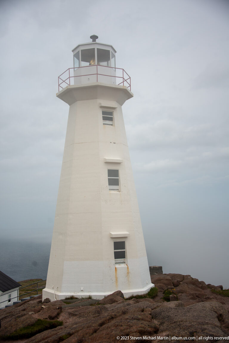 Full view of tapered white Cape Spear lighthouse tower with three windows, lantern room, and red gallery railing.