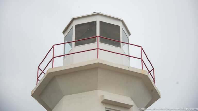 Close low-angle view of Cape Spear lighthouse lantern room and projecting gallery with red metal railing.