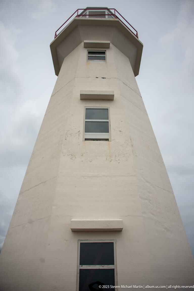 Low-angle view up the tapered white Cape Spear lighthouse tower toward windows, gallery, and lantern room.