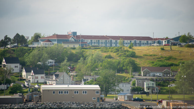Large red-roofed complex crowns a green hillside above small houses near the waterfront.
