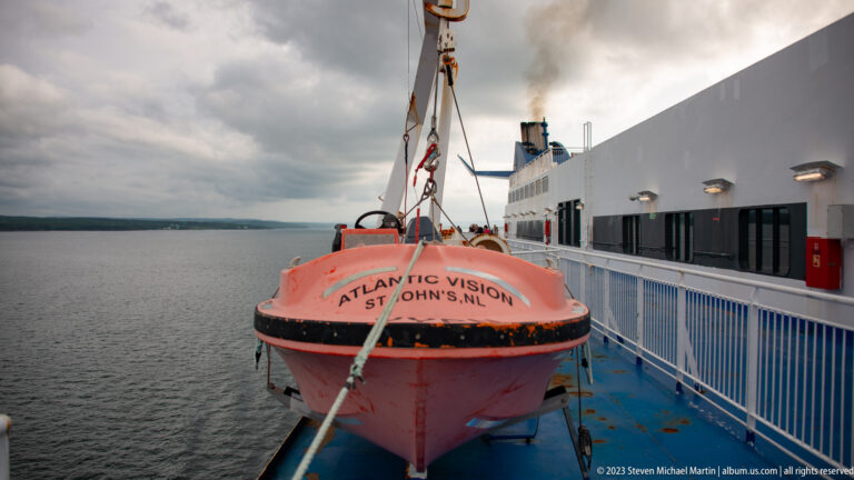 Orange enclosed lifeboat labeled Atlantic Vision and St. John's, NL hangs from davit gear along the ferry's side deck.
