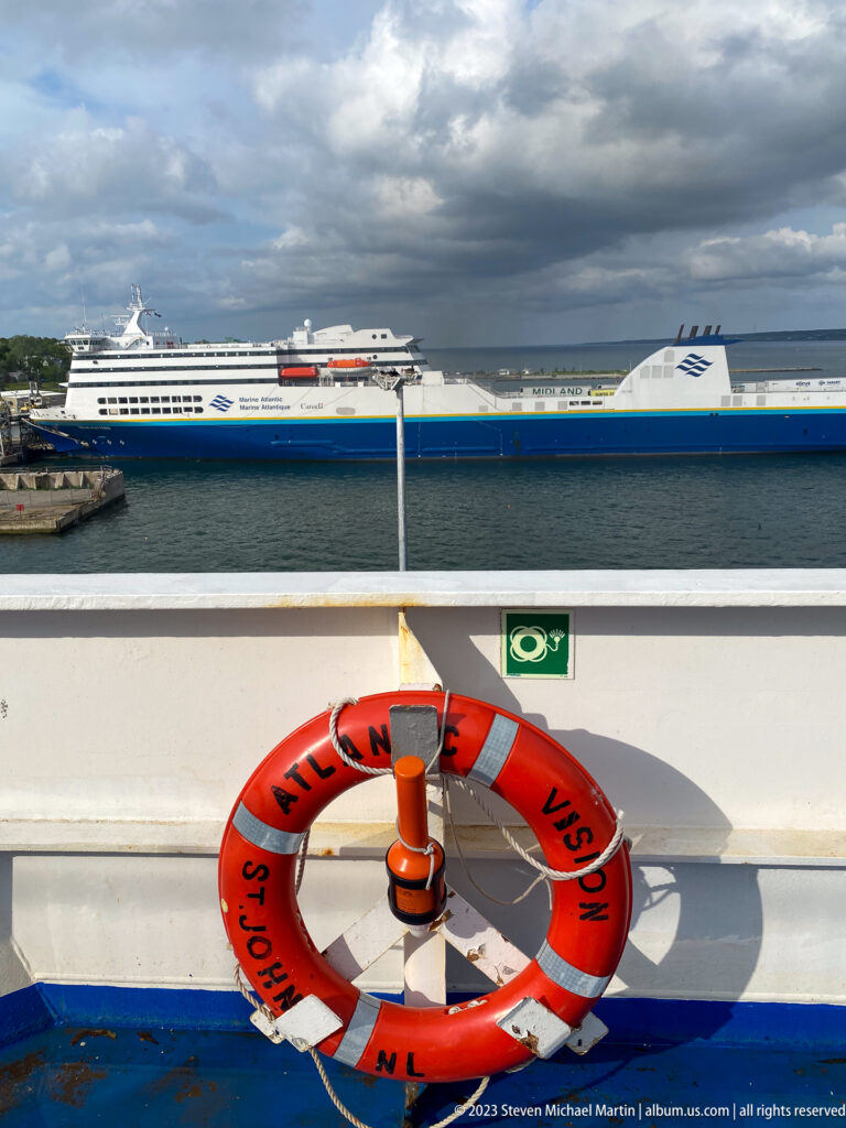Orange Atlantic Vision life ring on a ferry rail with a large blue-and-white Marine Atlantic ferry across the harbor.