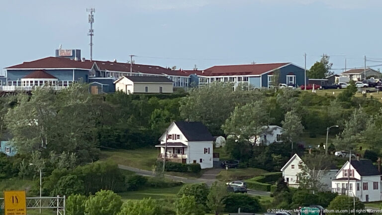 Long red-roofed complex tops a wooded hillside above detached houses descending toward the waterfront.
