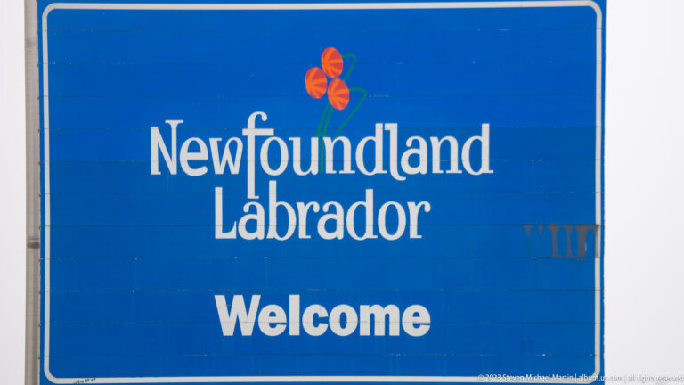 Close view of a blue Newfoundland and Labrador welcome sign with white lettering and provincial flower emblem.
