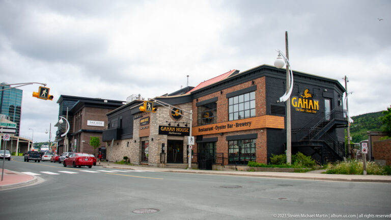 Corner view of Gahan House restaurant and brewery with dark siding, brick walls, exterior stairs, and yellow signs.