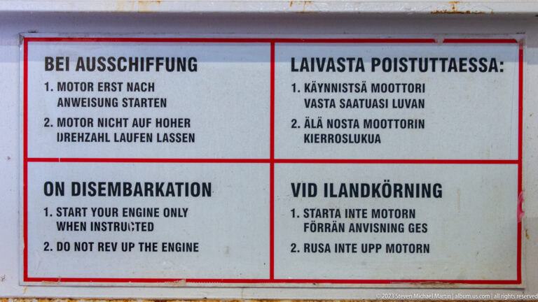 Red-bordered ferry sign with disembarkation engine instructions in German, Finnish, English, and Swedish.