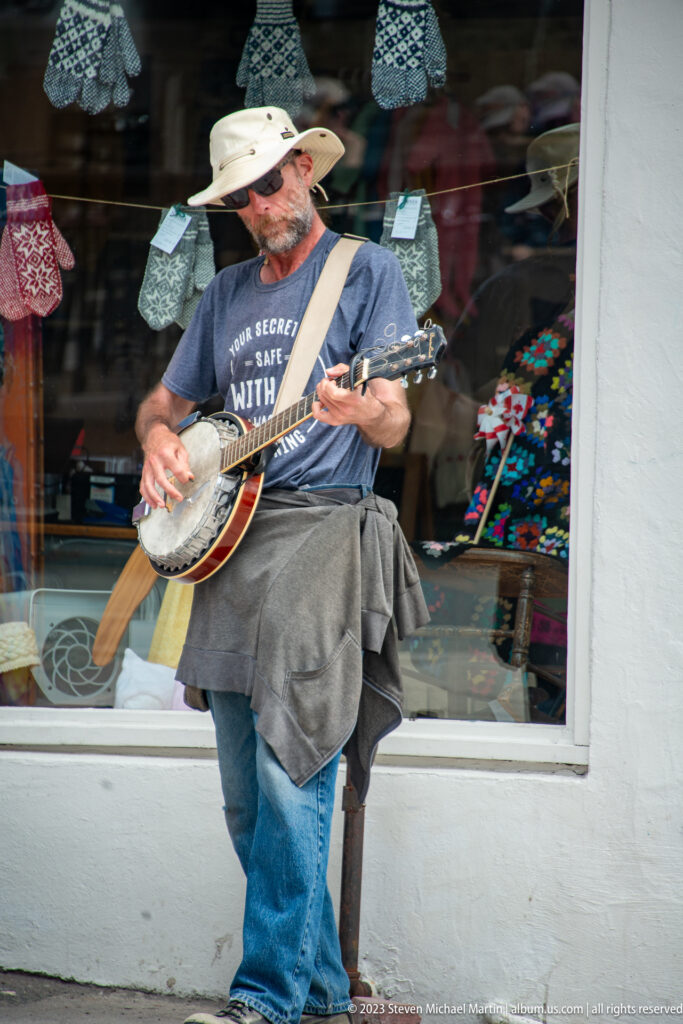 Street musician in a broad-brimmed hat plays banjo on a sidewalk in downtown St. John’s.