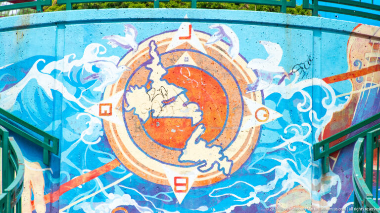 Colorful mural detail with stylized waves and a compass-like orange circle containing the outline of Newfoundland.