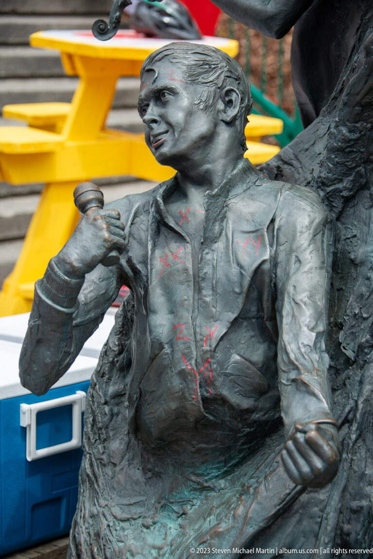 Close view of a bronze male performer leaning forward with a microphone in his hand.