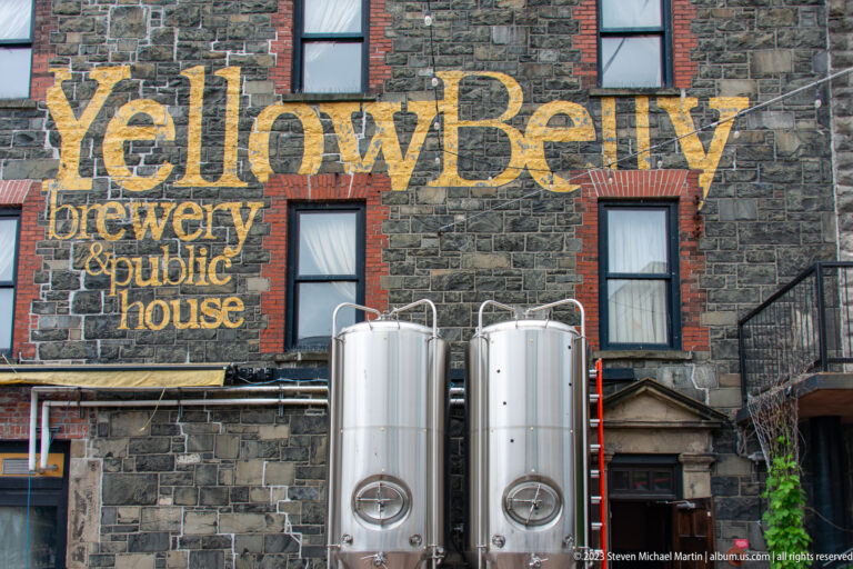 Two stainless-steel brewing tanks stand before the stone YellowBelly Brewery & Public House façade.
