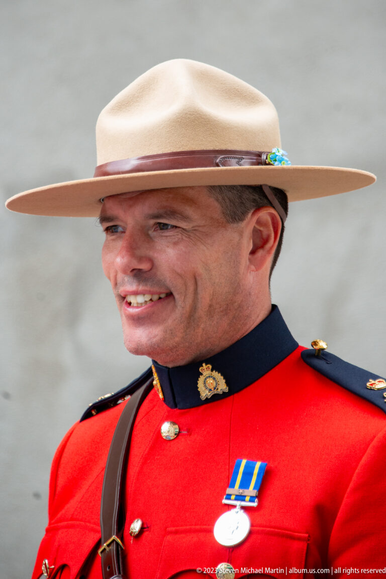 Close portrait of an RCMP officer wearing red serge, campaign hat, leather cross-strap, and a medal.