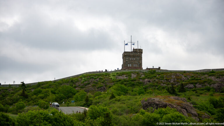 Cabot Tower stands on the green rocky summit of Signal Hill beneath an overcast sky.