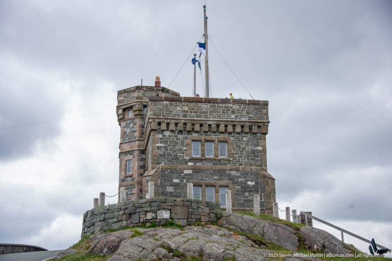 Close low-angle view of Cabot Tower’s gray stone walls, crenellated parapet, windows, and flag mast on Signal Hill.