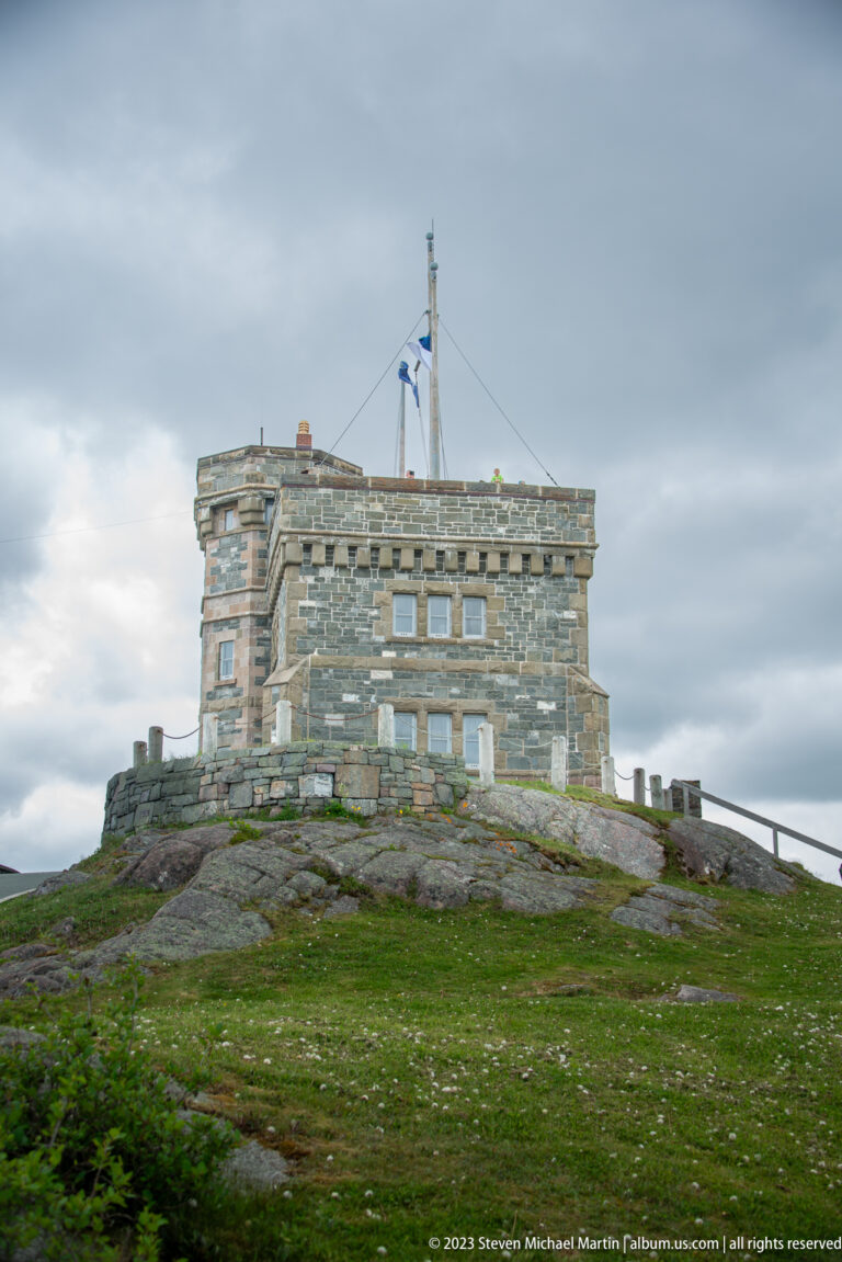 Cabot Tower stands on an open grassy and rocky Signal Hill summit beneath a gray sky.