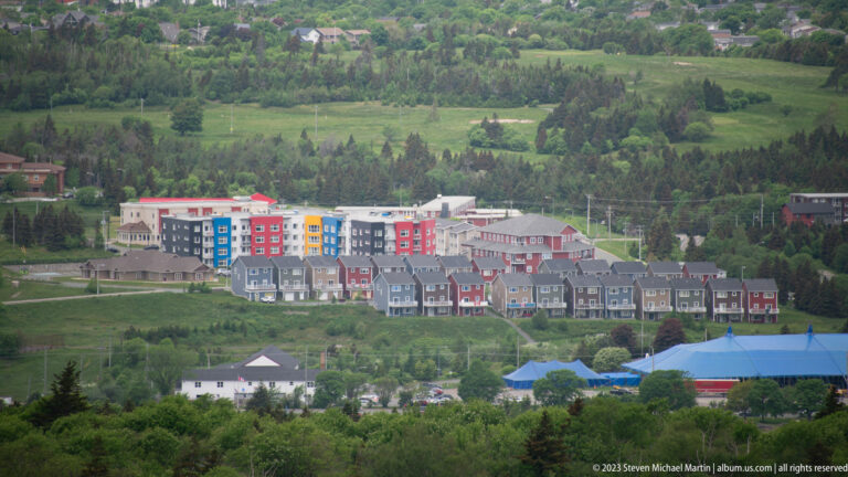 Modern townhouses and colorful apartment buildings spread across a green St. John’s hillside below Signal Hill.