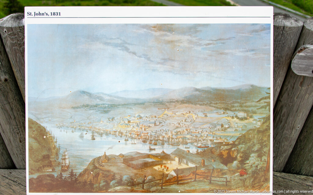 Historic illustrated panorama of St. John’s harbor crowded with ships, with the town spreading across steep surrounding hills.