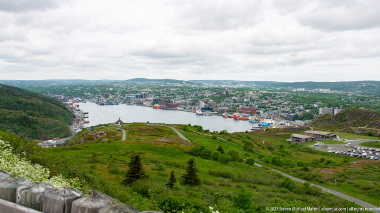 Elevated view from Signal Hill across green slopes to St. John’s harbor, waterfront vessels, and hillside neighborhoods.