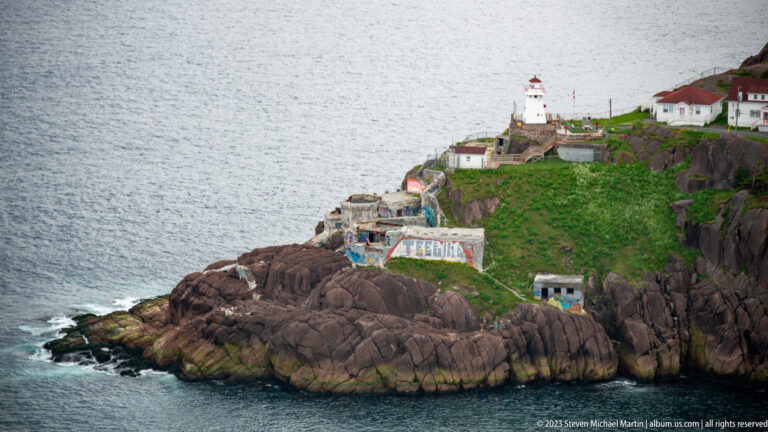 White Fort Amherst lighthouse and red-roofed buildings on rugged cliffs beside the entrance to St. John’s harbor.