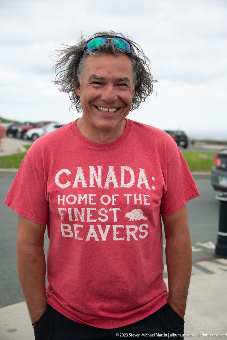 Smiling man outdoors wearing a red Canada T-shirt with the slogan “Home of the Finest Beavers.”