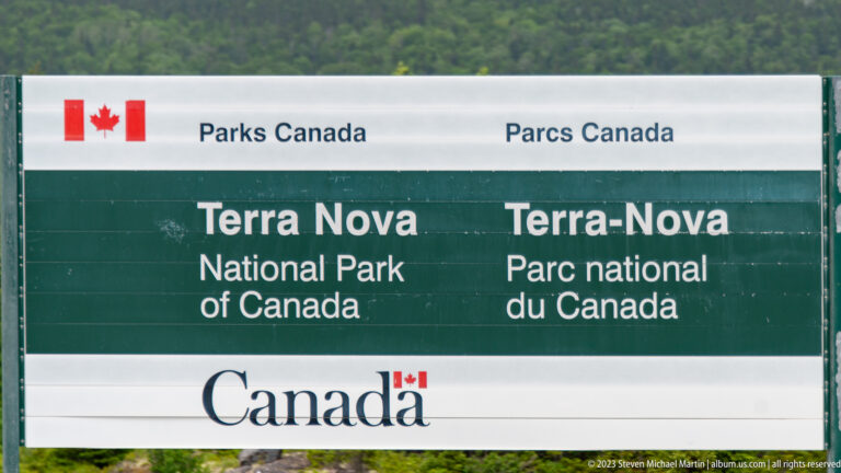 Bilingual Parks Canada entrance sign for Terra Nova National Park stands before dense green forest.