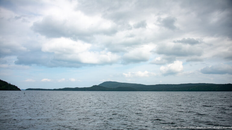 Open gray-blue water facing low forested islands beneath layered stormlike clouds.