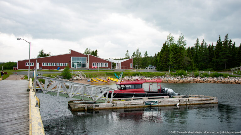 Red cabin boat moored at floating dock with visitor centre and kayaks across the harbour.