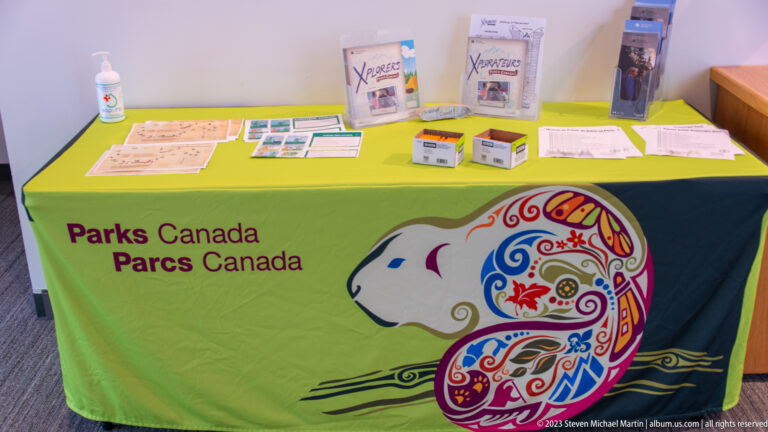 Parks Canada information table covered with a bright cloth and arranged with brochures, maps, and small boxes.