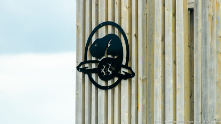 Dark circular wildlife emblem mounted on pale vertical wooden siding at a Parks Canada facility.