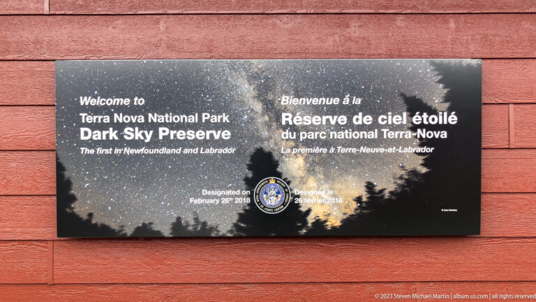 Black bilingual Dark Sky Preserve plaque on red siding with starry-sky imagery, emblem, and February 2018 designation.