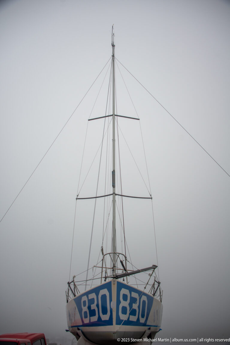 Head-on view of a hauled-out sailboat with blue-and-white bow marked 830 and mast rising into gray sky.