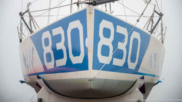 Close low-angle view of sailboat bow marked 830, showing the rounded hull underside and rigging above.