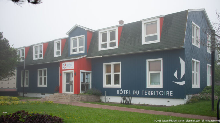 Dark blue Hôtel du Territoire with white-trimmed windows, dormers, red entrance and large white building name on the façade.