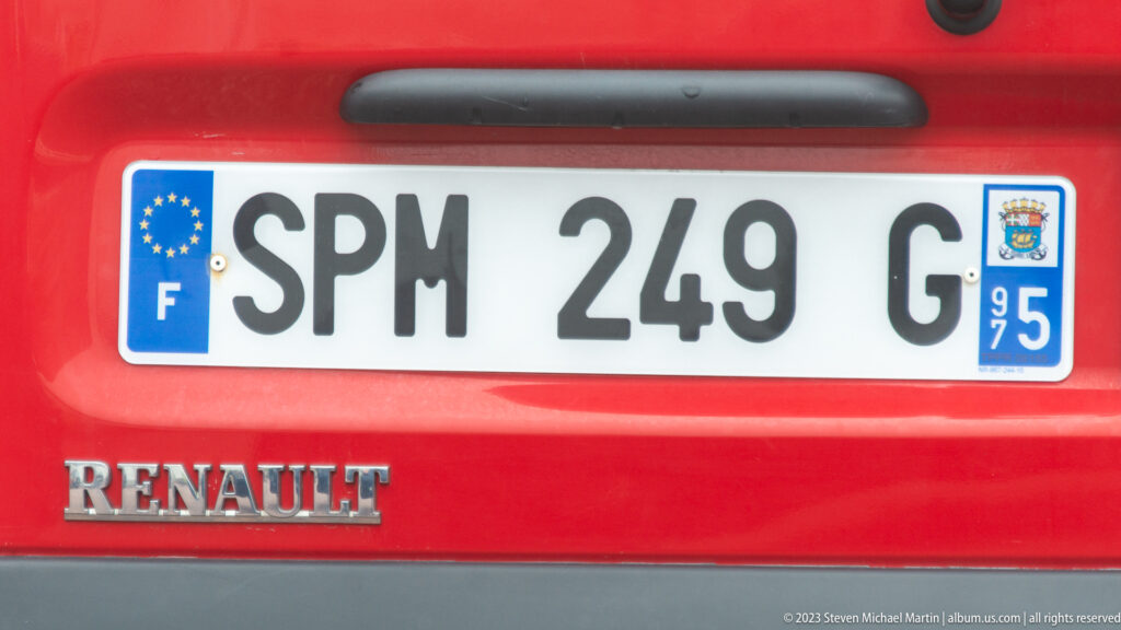 Close view of a red Renault with French plate “SPM 249 G” and a Saint-Pierre-et-Miquelon territorial emblem.