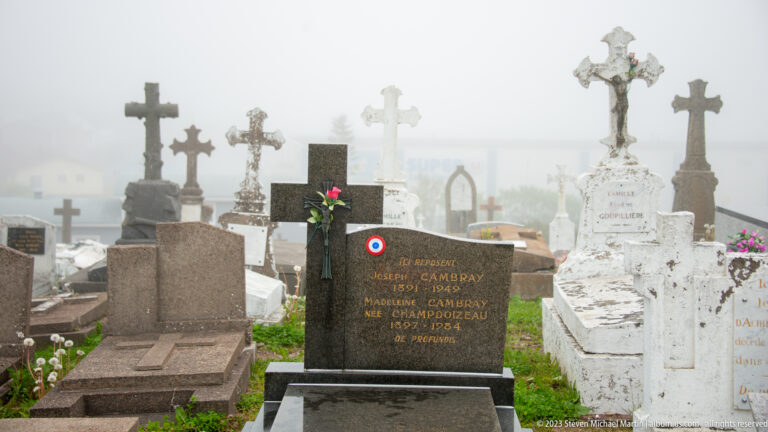 Dark grave marker for Joseph Cambray with a small French tricolor roundel, surrounded by crosses and white tombs.