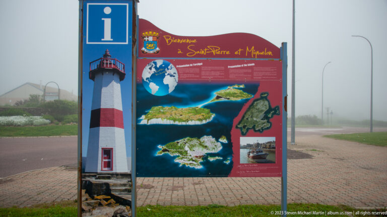 Welcome sign for Saint-Pierre-et-Miquelon with a lighthouse illustration, maps, aerial island views, and visitor information.