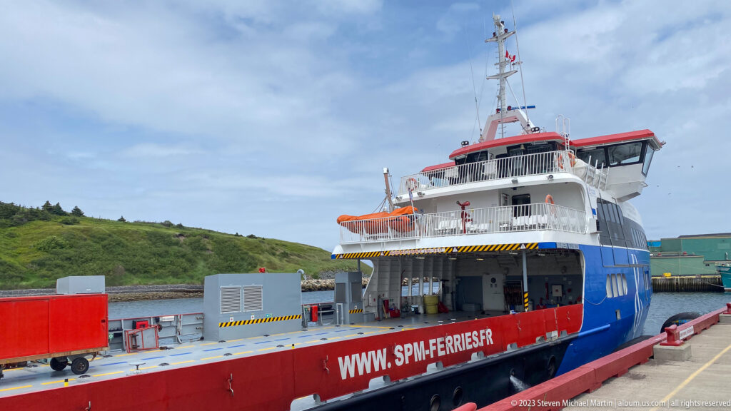 SPM Ferries roll-on/roll-off ferry moored stern-first beside a terminal, with vehicle deck and ramp area visible.