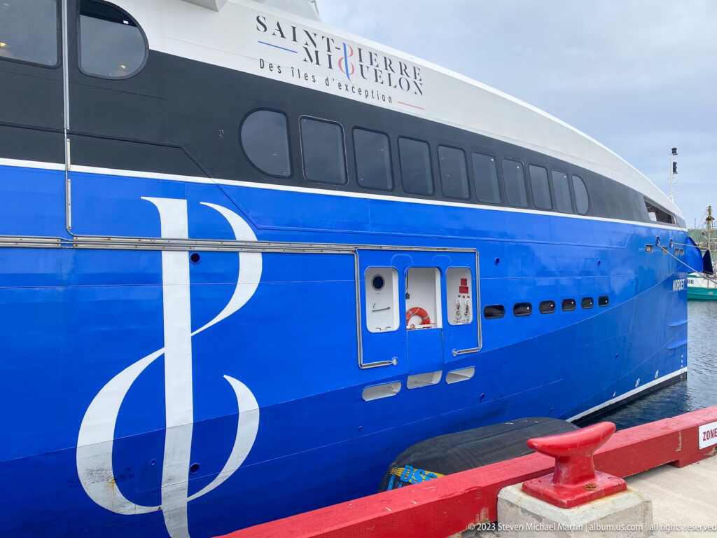 Large blue Saint-Pierre-et-Miquelon passenger ferry alongside a red quay, with rows of dark windows and territorial branding.