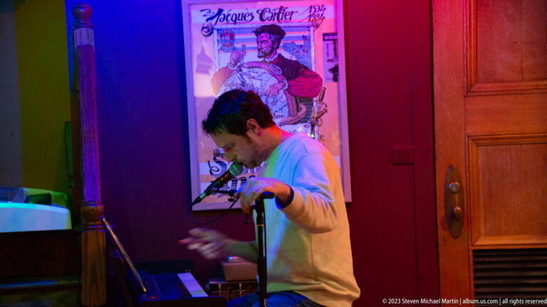Man playing an electronic keyboard in a small bar under blue, magenta, and green lighting.