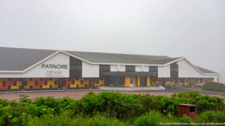 Saint-Pierre ice rink building marked PATINOIRE, with gray siding and orange, yellow, and red façade accents.