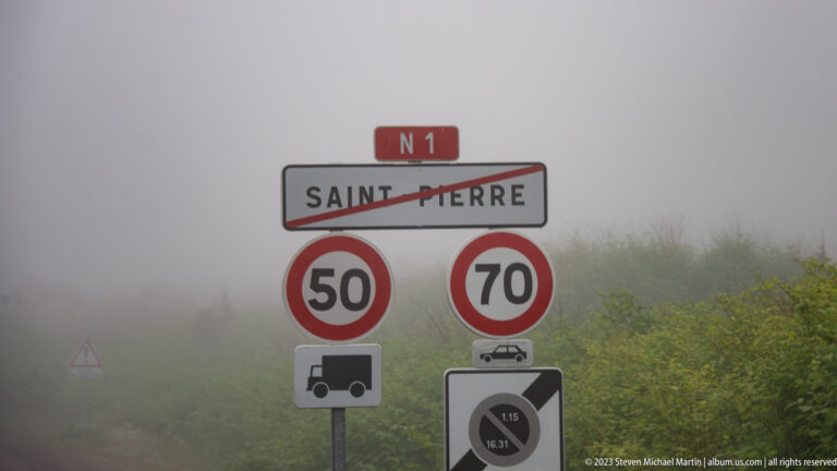 Route N1 sign with Saint-Pierre crossed out above 50 and 70 speed-limit signs in dense fog.