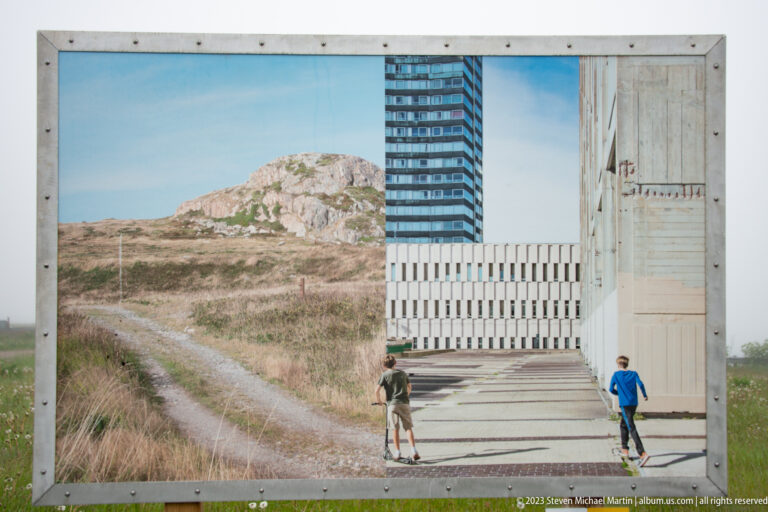 Outdoor panel showing a rocky rural track on the left and pedestrians among modern buildings on the right.
